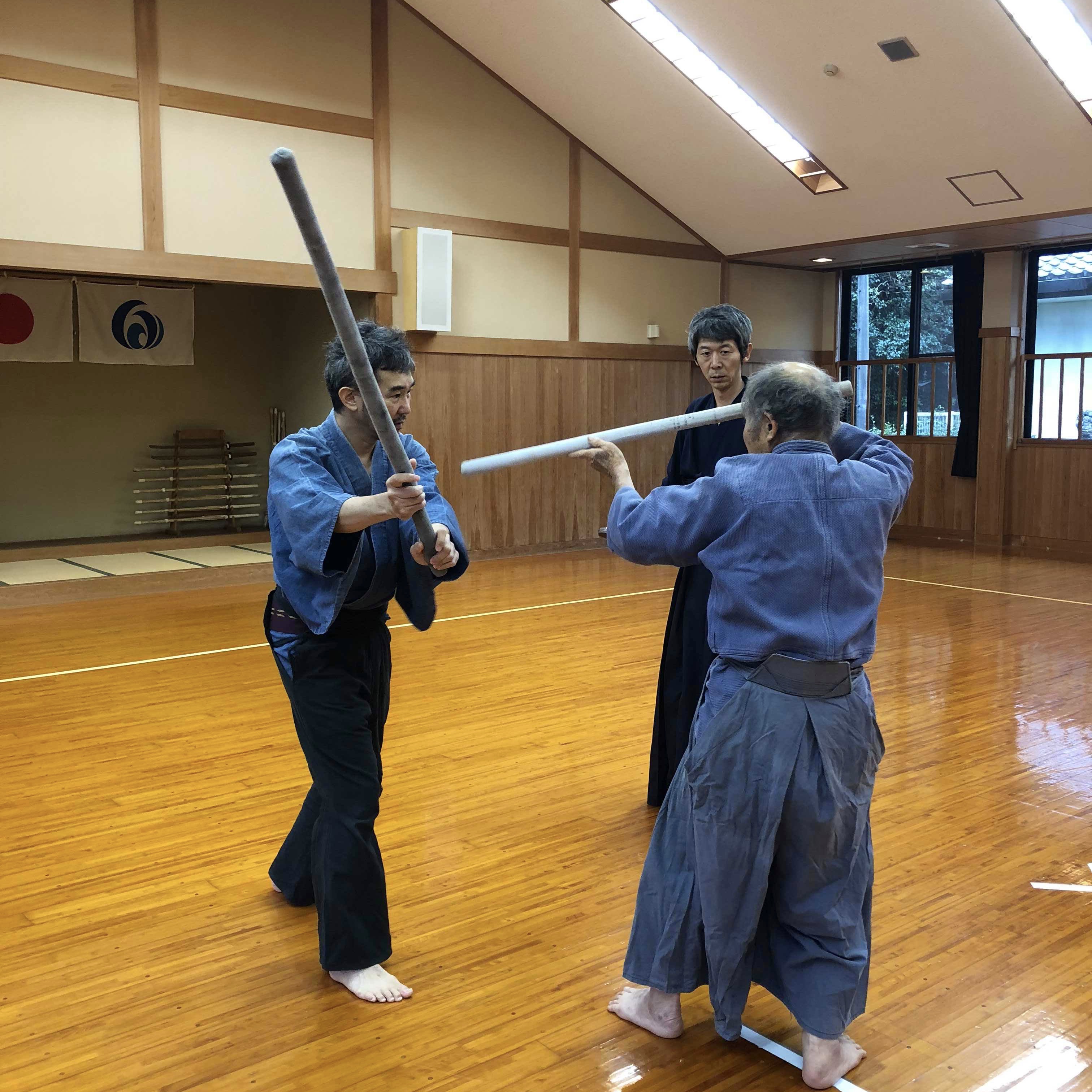 Mao Sasaki and Yamamoto-sensei holding long training implements in a dojo while another person observes
