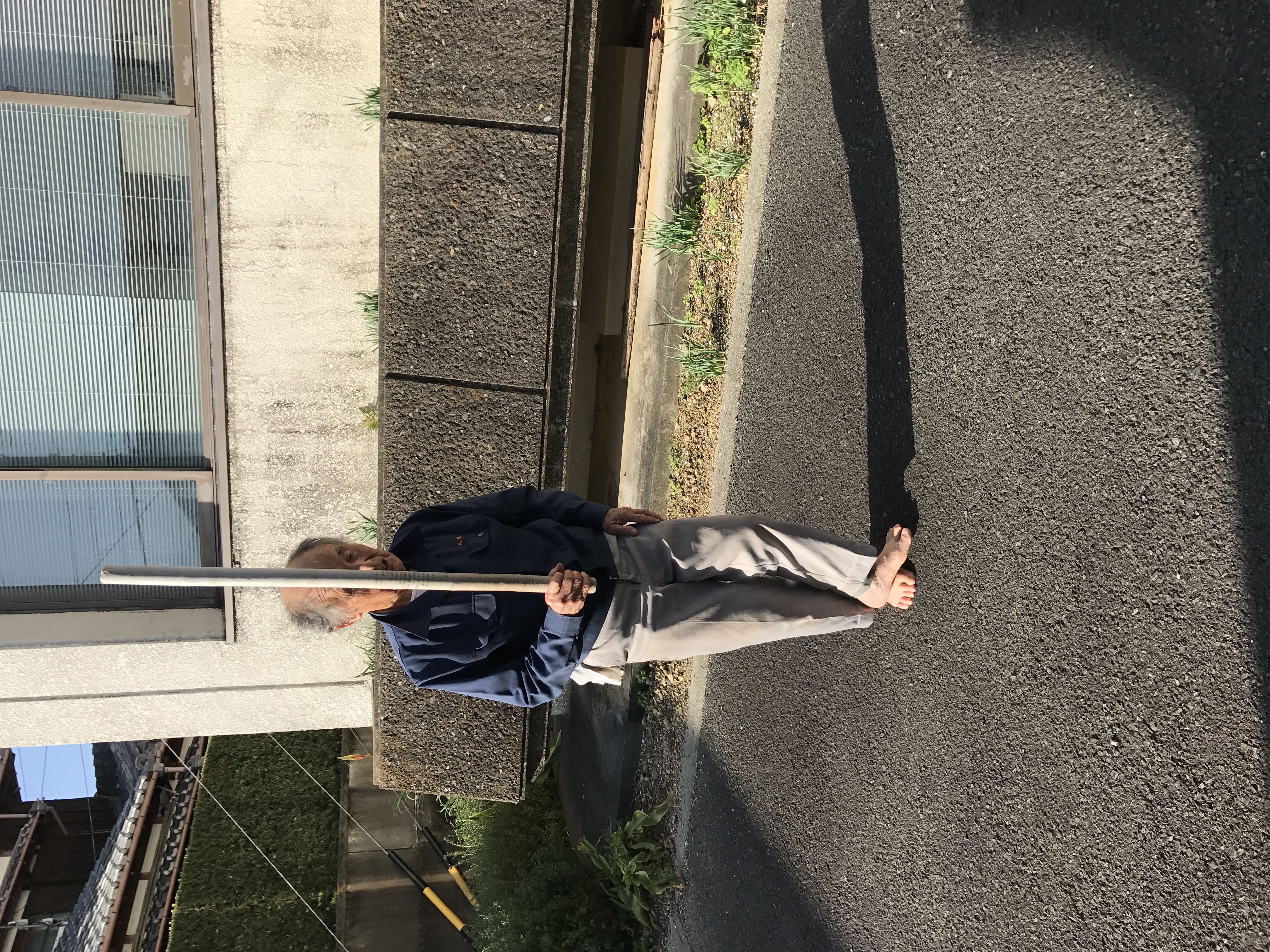 Yamamoto Atsushi standing outdoors in Gokasho in everyday clothes, holding a training implement